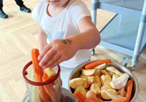 Dziewczynka wkłada marchewkę do otworu sokowirówki