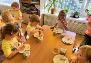 Dzieci siedzą przy stoliku i smakują sałatkę