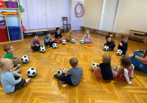Każde dziecko siedzi na podłodze a przed nim leży talerzyk na nim piłką