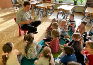 Dzieci siedzą na podłodze i słuchają jak pan czyta książkę