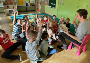 Dzieci siedzą i podnoszą rękę do góry jako znak zgłoszenia się do odpowiedzi