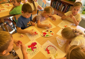 Dzieci siedzą przy stole i malują obrazek z Indykiem
