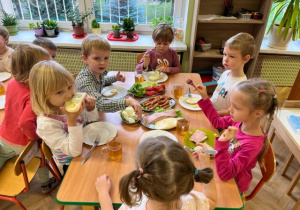Dzieci siedzą przy stole i nakładają na chlebek serek