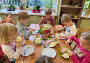 Dzieci siedzą przy stole i jedzą z apetytem zdrowe kanapki