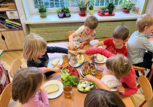 Dzieci nakładają na chleb wędlinę i ser zółty
