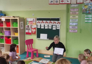 Dzieci siedzą na dywanie a nauczyciel pokazuje obrazek z sylabą