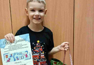 Chłopiec pozuje do zdjęcia z dyplomem wyróżnienia w konkursie plastycznym