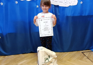 Dziewczynka pozuje do zdjęcia z dyplomem zdobycia I miejsca w konkursie plastycznym