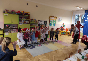 Dzieci stoją na środku sali i śpiewają piosenkę z nauczycielką.