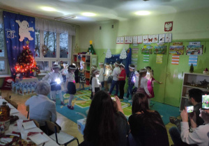Dzieci tańczą w kole trzymając małe latarki