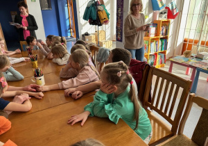 Dzieci siedzą przy stole i słuchają opowiadania o życiu Dinozaurów
