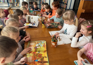 Dzieci siedzą przy stole i oglądają książeczki o życiu Dinozaurów