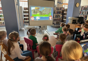Dzieci siedzą na krzesełkach i oglądają film edukacyjny o Dinozaurach