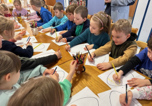 Dzieci siedzą przy stole i kolorują pisankę