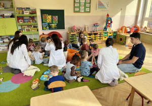 Dzieci siedzą na dywanie ze Studentami i badają misie