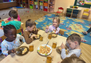 Dzieci siedzą przy stole - jedzą sałatkę i pija herbatkę