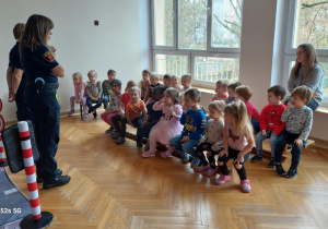 Dzieci siedzą na ławeczkach a Panie ze Straży Miejskiej objaśniają zasady zabawy