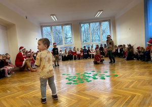 Chłopiec stoi na środku i zadaniem jego jest pozbiera z podłogi jak najwięcej choinek na dany sygnał