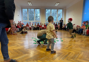 Chłopiec stoi na środku i zadaniem jego jest pozbiera z podłogi jak najwięcej choinek na dany sygnał