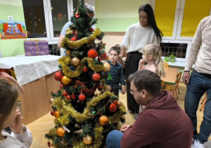 Rodzice i dzieci dekorują choinkę ozdobami