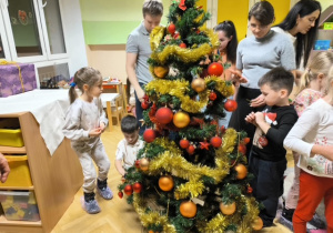 Rodzice i dzieci dekorują choinkę ozdobami