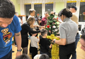 Rodzice i dzieci dekorują choinkę ozdobami