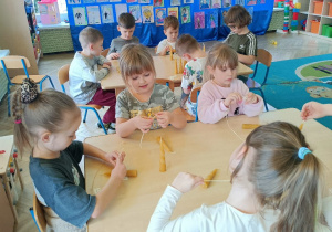 Dzieci przekładają rafię przez wizytówkę i zawiązują ją na świeczce