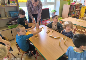 Dzieci siedzą przy stoliku i robią świece z wosku