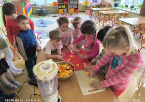 Dzieci ostrożnie kroją warzywa i owoce nożem plastikowym ma desce