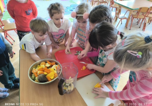 Dzieci ostrożnie kroją warzywa i owoce nożem plastikowym ma desce