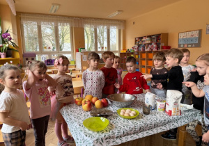 Dzieci stoją przy stole na którym znajdują się produkty do wykonania szarlotki