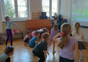 Dzieci wykonują ćwiczenia pokazywane na ekranie tablicy multimedialnej