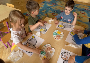 Dzieci siedzą przy stoliku i malują farbami