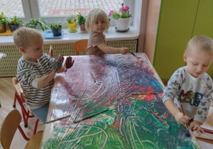 Dzieci malują farbami na stole na folii pędzelkiem lub rękoma
