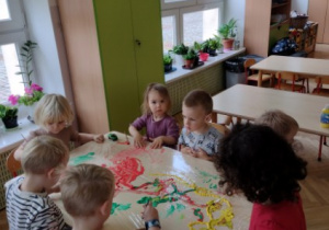 Dzieci siedzą przy stole i malują farbami