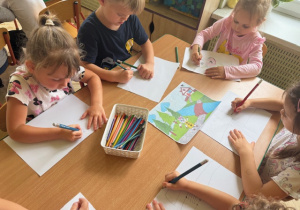 Dzieci siedzą przy stole i rysują ilustrację do bajki