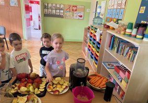Dzieci wkładają jabłka i marchewkę do sokowirówki