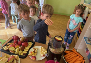 Chłopiec wkłada jabłka i marchewkę do sokowirówki
