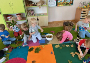 Dzieci siedzą na dywanie i oglądają dary jesieni - kolorowe liści i kasztany