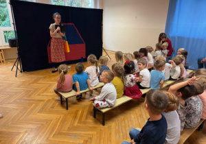 Dzieci siedzą na ławeczkach a pani opowiada o podróży