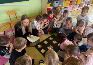 Dzieci siedzą na dywanie i wyszukują te ilustracje pasujące do opowiadania