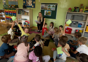 Dzieci siedzą w małych grupkach i podnoszą rękę z kartką