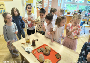 Dzieci stoją przy stole i jedzą pieczywo z dżemem lub miodem