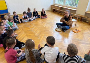 Dzieci siedzą w kole na podłodze i słuchają o życiu lotopałanki