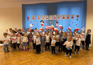 Dzieci stoją machają chorągiewkami i śpiewają piosenkę