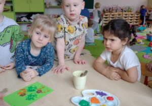 Dzieci przy stoliku pieczętują farbami swoją pocztówkę