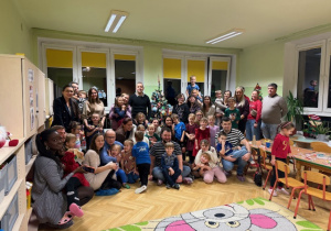 Dzieci i rodzice pozują do zdjęcia przy dekorowanej choince