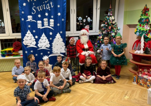 Dzieci siedzą na podłodze wspólnie z Mikołajem przy choince