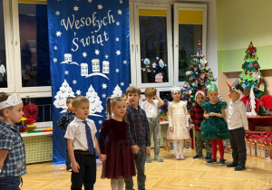Dzieci stoją na środku sali i recytują wiersz o tematyce świątecznej