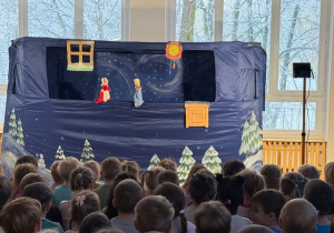 Dzieci siedzą na ławeczkach i oglądają teatrzyk kukiełkowy